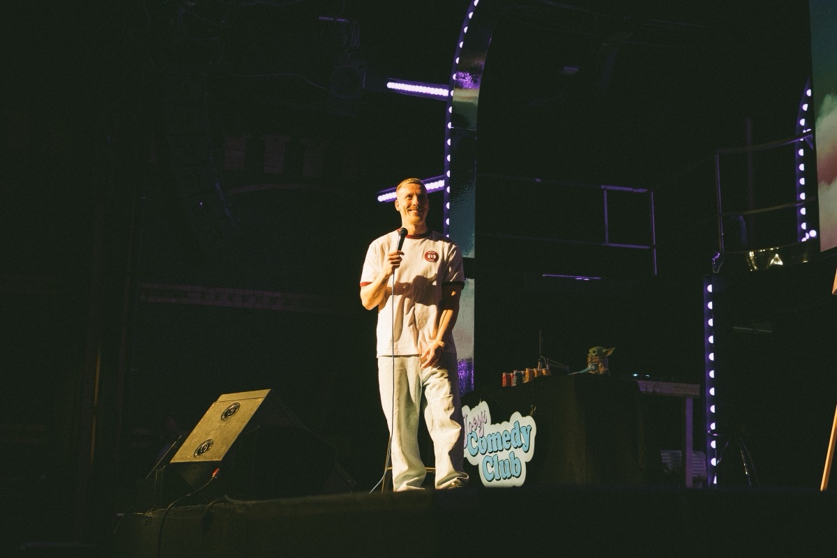 Comedian mit Mikrofon auf der Bühne, daneben ein Schild mit dem Schriftzug Joey's Comedy Club