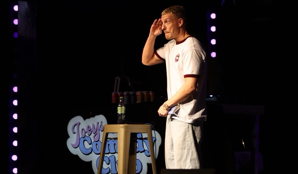Felix Lobrecht auf der Bühne, daneben das Schild von Joey's Comedy Club